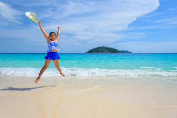 Fototapeta na wymiar Tourist girl in a blue white striped swimsuit jumping shaped X with happy on the beautiful beach and sea during summer at Koh Miang Island, Mu Ko Similan National Park, Phang Nga province, Thailand