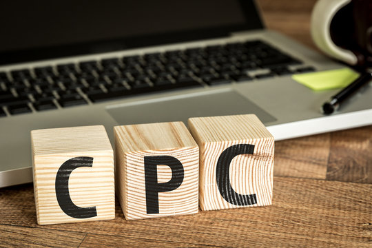 CPC (Cost Per Click) written on a wooden cube in front of a laptop