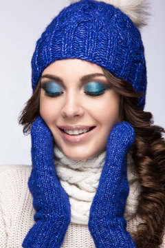 Beautiful girl with brightmakeup, curls and smile in blue knit hat. Warm winter image. Beauty face.