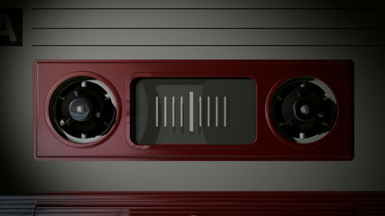 A macro static camera view of a red vintage audio cassette tape with a white label in use playing back in a cassette player in a dark environment