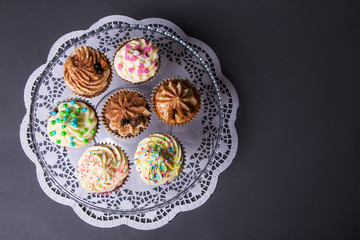 close up of sweet colorful cupcakes on glass plate over gray