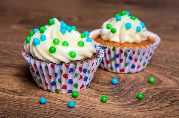 two sweet cupcakes with butter cream on wooden table