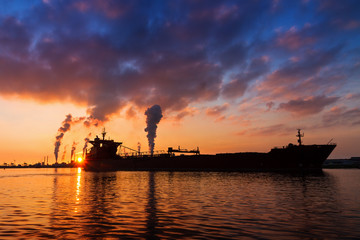 Obraz premium Silhouette of a big cargo ship and industry at sunset in IJmuiden in the Netherlands