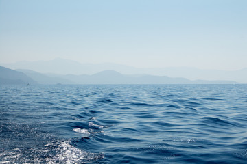 Seascape with distant mountains, sky and wavy sea water