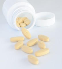 Yellow pills and white bottle with lid on white background