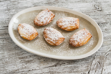 cookies madeleines with powdered sugar on oval plate on a light wooden surface