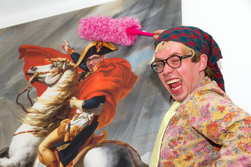 Jolly young man dusting off a large portret of himself as Napoleon during the spring clean up in the house