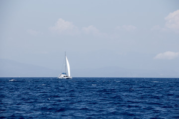 Obraz premium Seascape sailing boat, distant mountains and fluffy clouds
