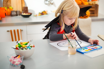 Interested halloween dressed girl drawing pumpkin Jack-O-Lantern