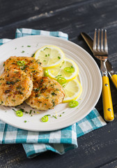 chicken cutlets with lemon and herbs on a white plate on a dark wooden background