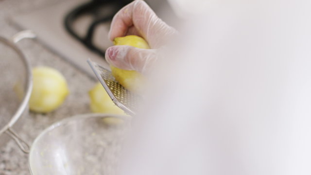 4K Over the shoulder view of a lemon being used on a zester to remove the rind