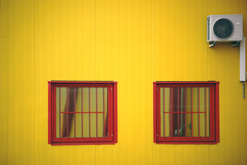 Obraz na płótnie Canvas Vergitterte Fenster mit Lüfter / Die gelbe Seitenwand eines Einkaufszentrums mit vergitterten Fenstern 