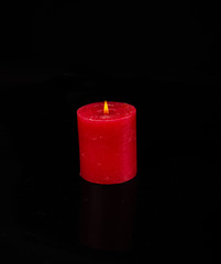 A single burning red candle isolated in front of black backgroun