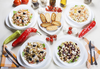 Four delicious salads of various vegetables and toast bread arranged on the table with fresh garlic, peppers, tomatoes, spices and seasoned oil.