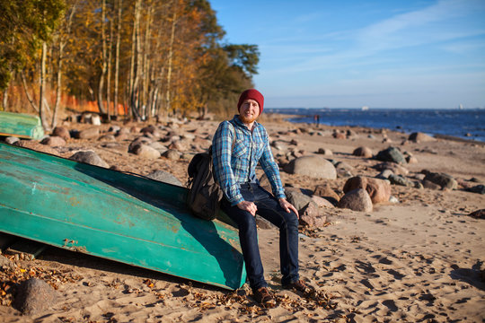 a man with a backpack sitting in a boat on a rocky beach in autumn