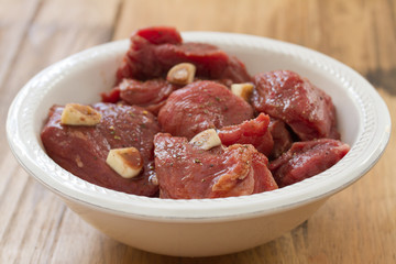 marinated meat in white plate on brown wooden background