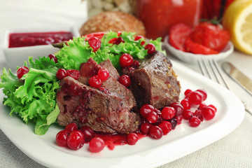 Tasty roasted meat with cranberry sauce on plate, on light background