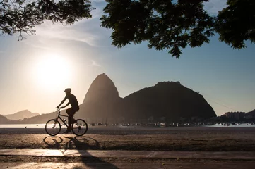 Fotobehang Silhouet van een man fietsen in de vroege ochtend tijdens mooie warme zonsopgang in Rio de Janeiro © Donatas Dabravolskas