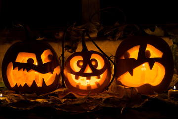 Photo composition from three pumpkins on Halloween. Embittered, mad and afraid of some pumpkin against an old window, leaves and candles.