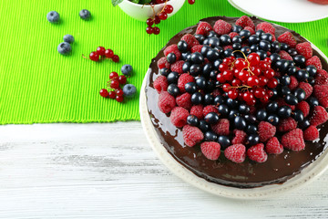 Delicious chocolate cake with summer berries on wooden table with green napkin, closeup