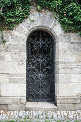 Old medieval black metal door with cerved bar and light stone