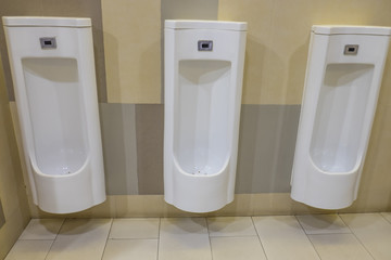 Closeup of three white urinals in men's bathroom.