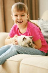 Little cute girl playing with kitten on sofa at home