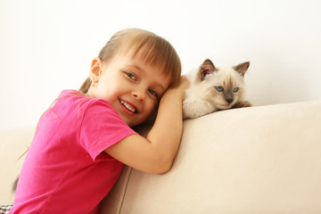 Fototapeta na wymiar Little cute girl with kitten on sofa at home
