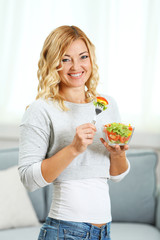 Beautiful woman with salad on home interior background