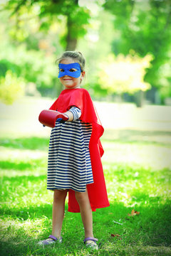 Happy little girl dressed as superhero in boxing gloves at the park