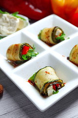 Zucchini rolls with cheese, bell peppers and arugula on plate, close-up, on table background