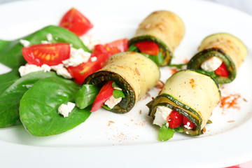 Zucchini rolls with cheese, bell peppers and arugula on plate, close-up, on table background