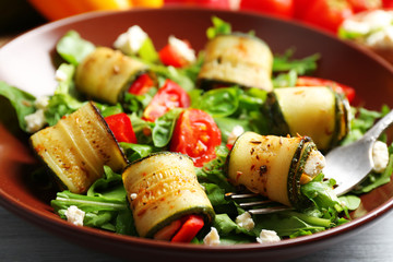 Salad with arugula and zucchini rolls on plate, on table background