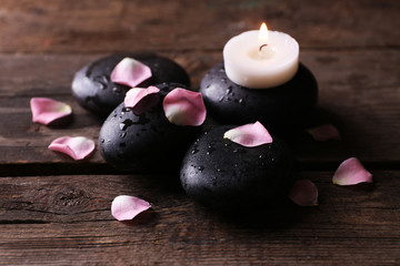 Alight candle and pebbles covered with rose petals on wooden background