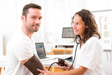 Obraz premium Young attractive doctor checking patient's blood pressure