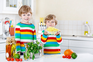 Two little kid boys eating spaghetti in domestic kitchen.