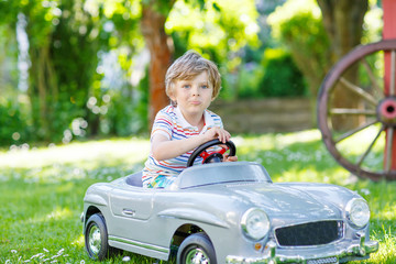 Kid boy driving with big toy car outdoors