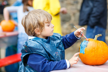 Fototapeta premium Little kid boy painting with colors on pumpkin