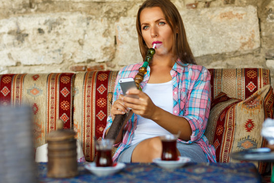 Woman smoking a hookah and uses smartphone in a cafe in Istanbul