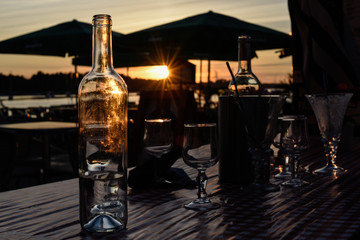 Bottle with vater and wine glasses on the table, at sunset