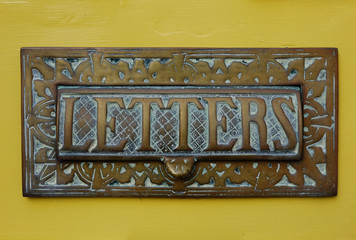 Letters aged brass sign and flap on yellow door