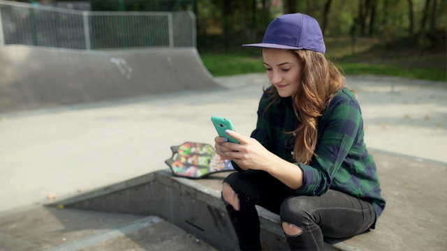 Girl wearing purple cap and using smartphone in skate park
