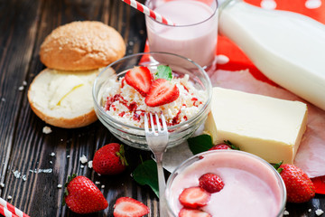 healthy breakfast of fruit and dairy products , cottage cheese with sour cream and milk, butter and roll , strawberries and syrup on a wooden background