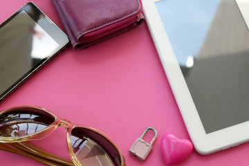 Set of woman's everyday objects - smartphone, wallet, tablet computer, sunglasses, padlock and heart on pink background - copy space