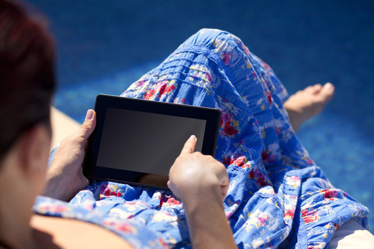 carefree woman uses touch pad tablet technology at the poolside