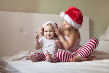 Children in pajamas and Christmas caps playing on the bed