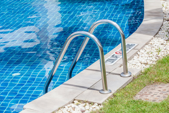 The view of metallic ladder entrance to clear blue swimming pool