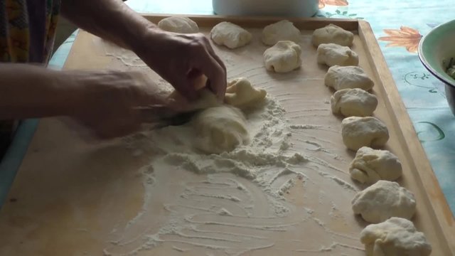 An elderly woman cut dough for pies