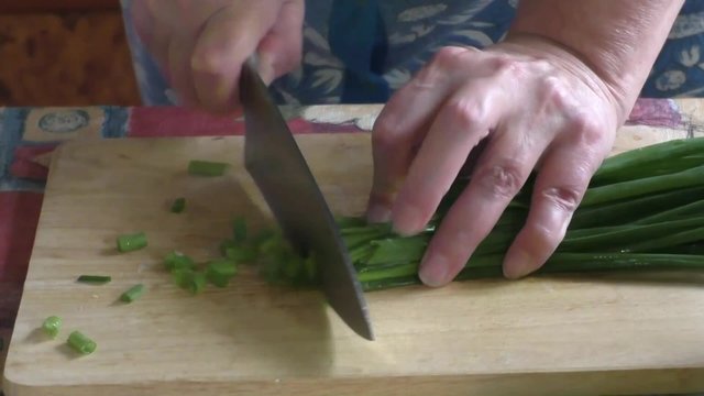 Woman cut green onions on a wooden cutting board