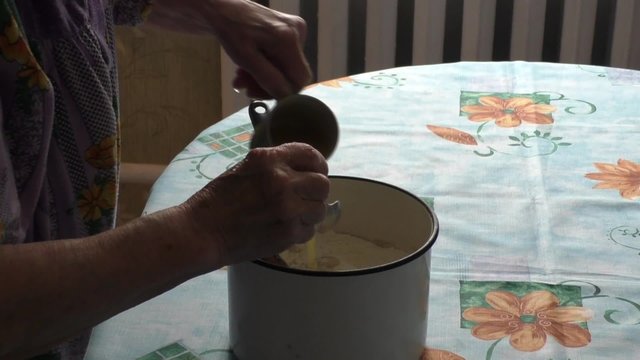 Elderly Woman adds to the dough egg